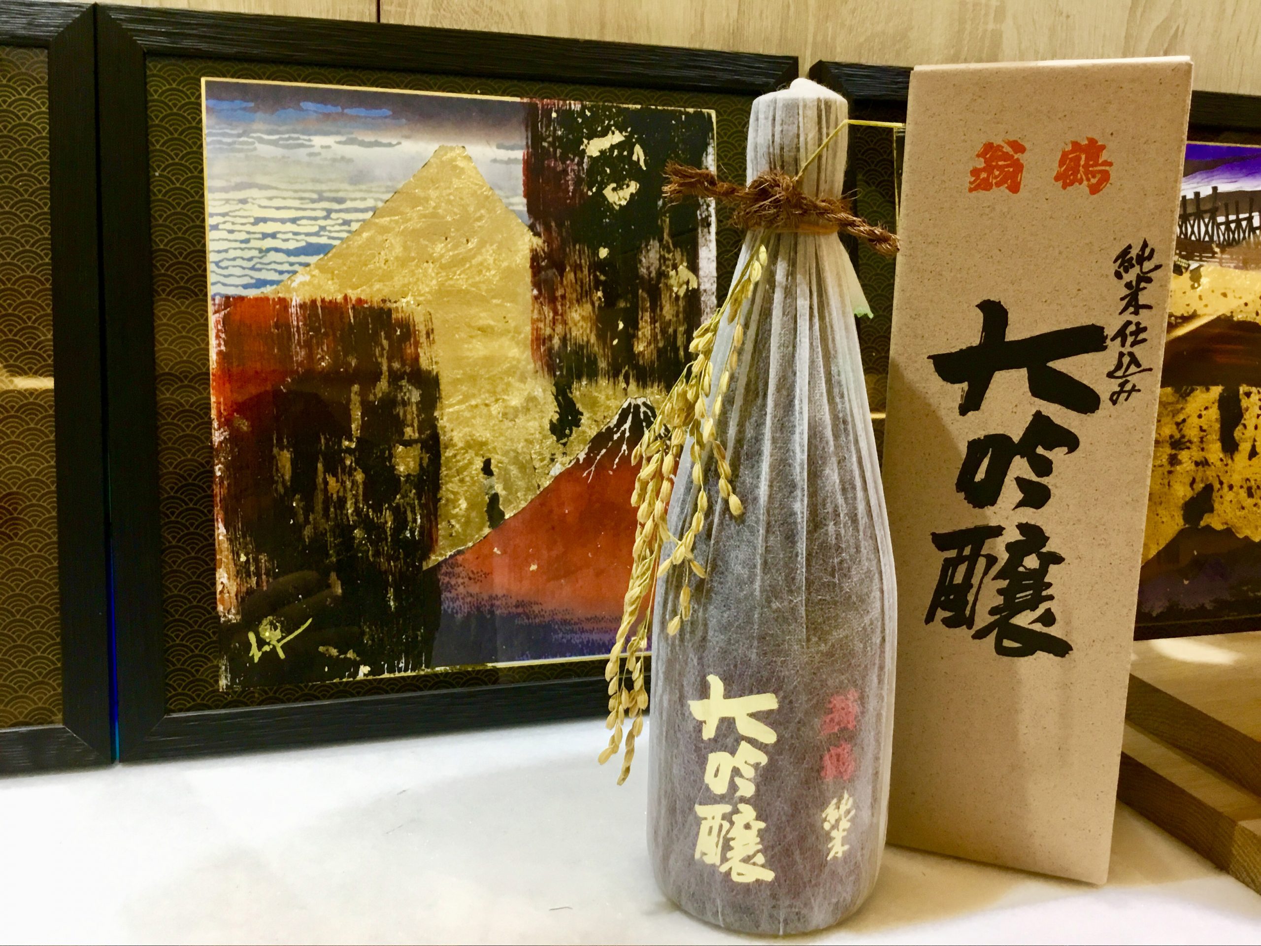 Bouteille de saké dans son emballage devant une peinture